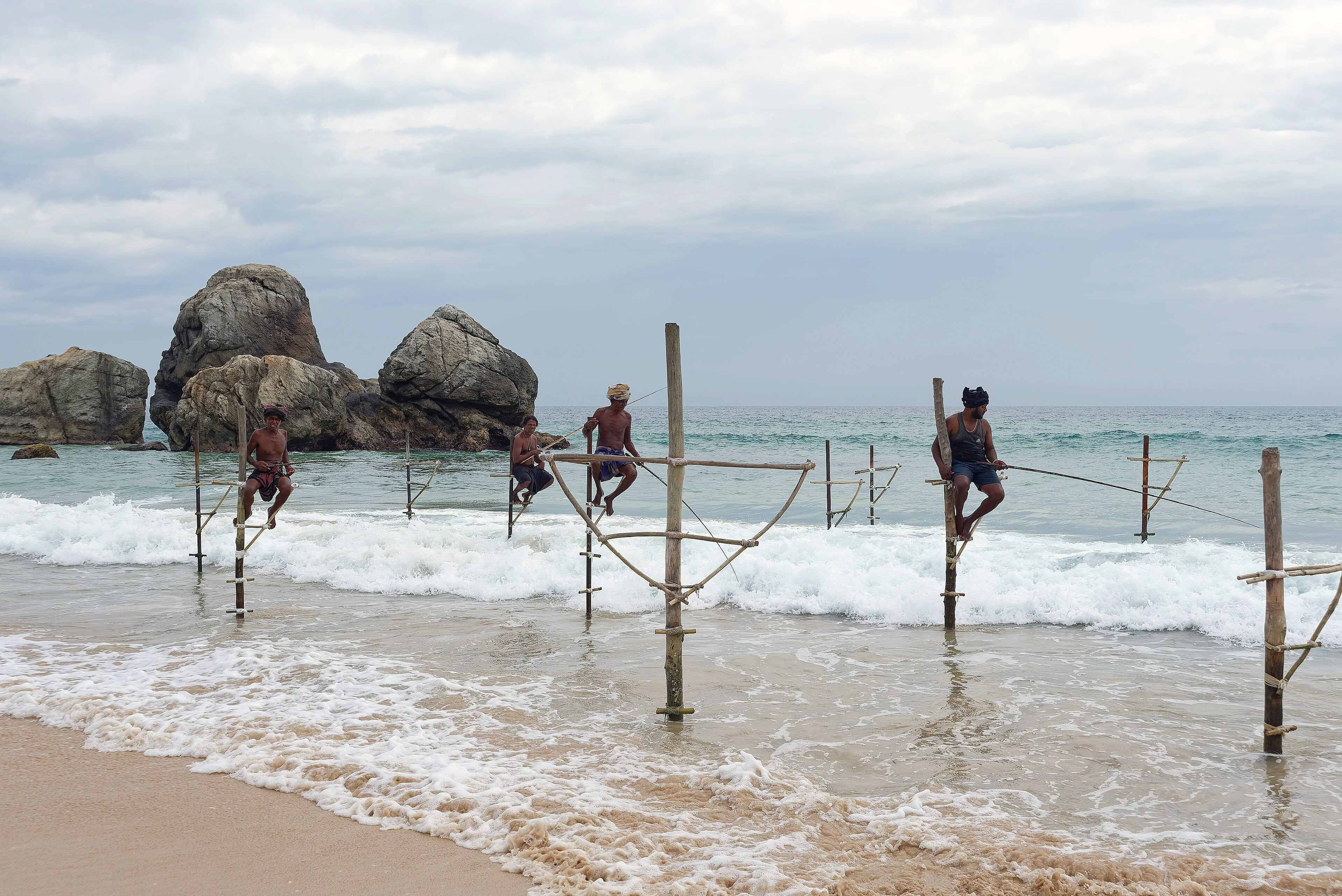 Stilt fishermen perched on poles in the surf near Galle