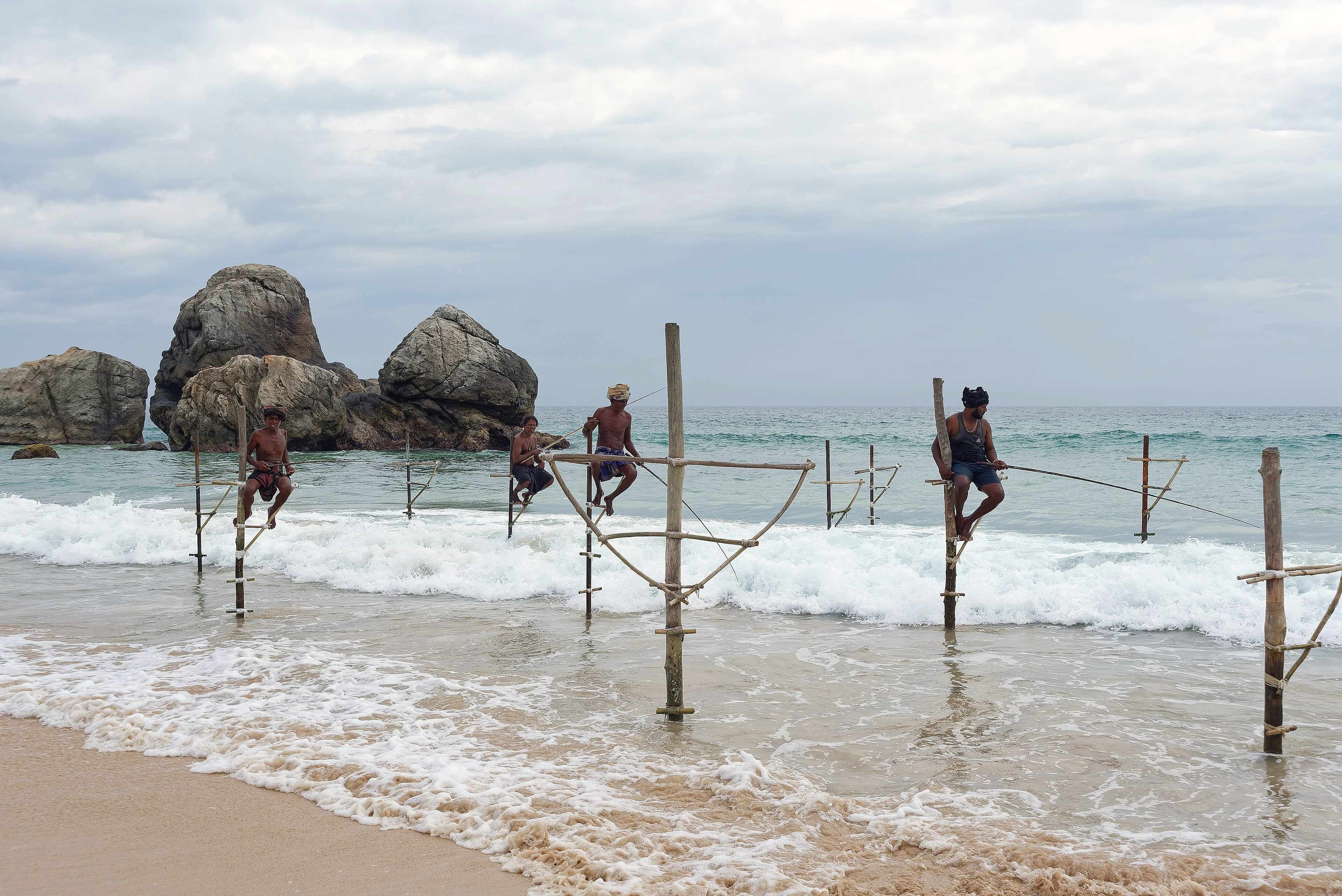 Stilt fishermen perched on poles in the surf near Galle